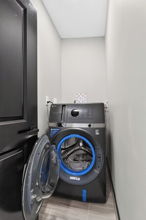 A compact, modern laundry room with a front-loading washer and dryer, a black cabinet, and a tiled floor.