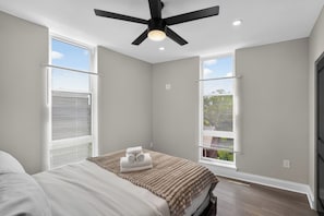 A bedroom with a bed, a ceiling fan, and two windows with blinds. - Queen Village Grand | 3BR, Rooftop & Garage (Philadelphia)