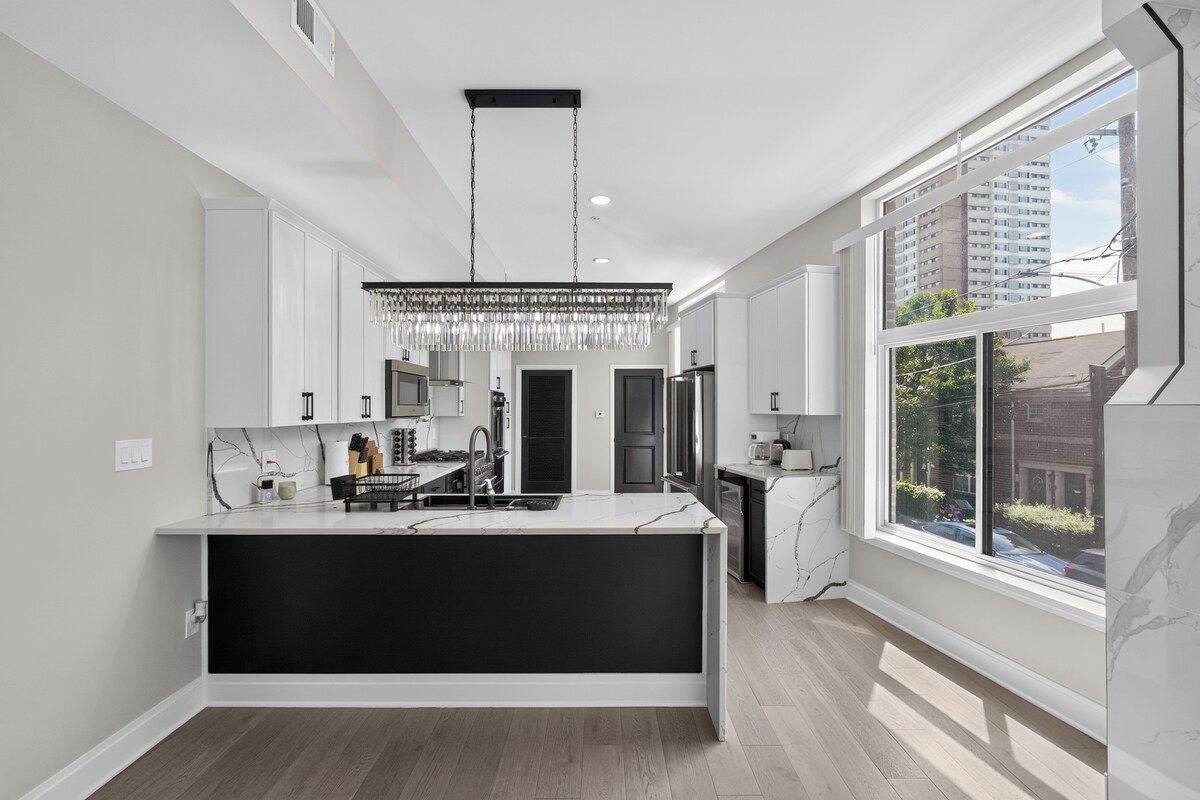 A modern kitchen with a central island, white cabinetry, and a large window providing a view of the outside.
