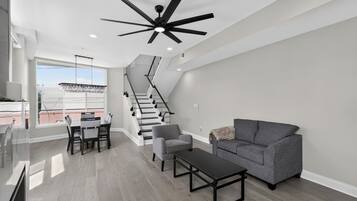 A modern living room with a staircase, a dining area, and a ceiling fan.