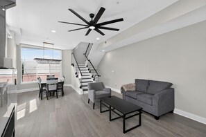 A modern living room with a staircase, a dining area, and a ceiling fan. - Queen Village Grand | 3BR, Rooftop & Garage (Philadelphia)