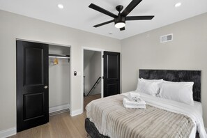 A bedroom with a bed, a ceiling fan, and a door leading to a hallway.