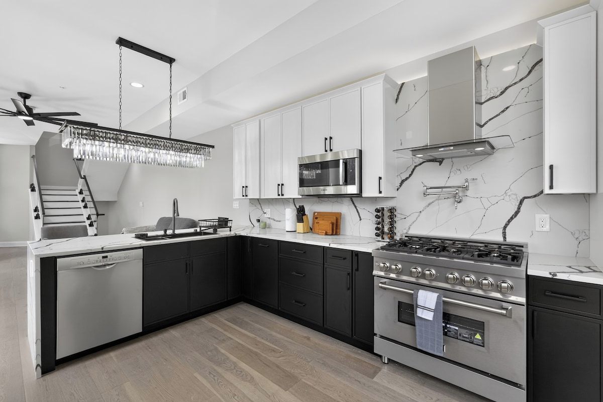 A modern kitchen with a dishwasher, stove, microwave, and marble backsplash.