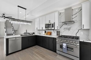 A modern kitchen with a dishwasher, stove, microwave, and marble backsplash. - Queen Village Grand | 3BR, Rooftop & Garage (Philadelphia)