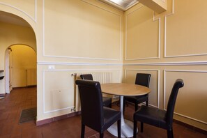 Un coin repas avec une table ronde et quatre chaises, un radiateur et une porte donnant sur une autre pièce.