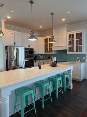 A modern kitchen with white cabinets, stainless steel appliances, and teal bar stools. - Seas The Day Navarre (Navarre)