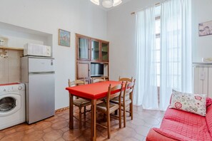 Ein kompakter Wohnraum mit Esstisch, Stühlen, einer Waschmaschine, einem Kühlschrank, einem Schrank mit Fernseher und einem roten Sofa.