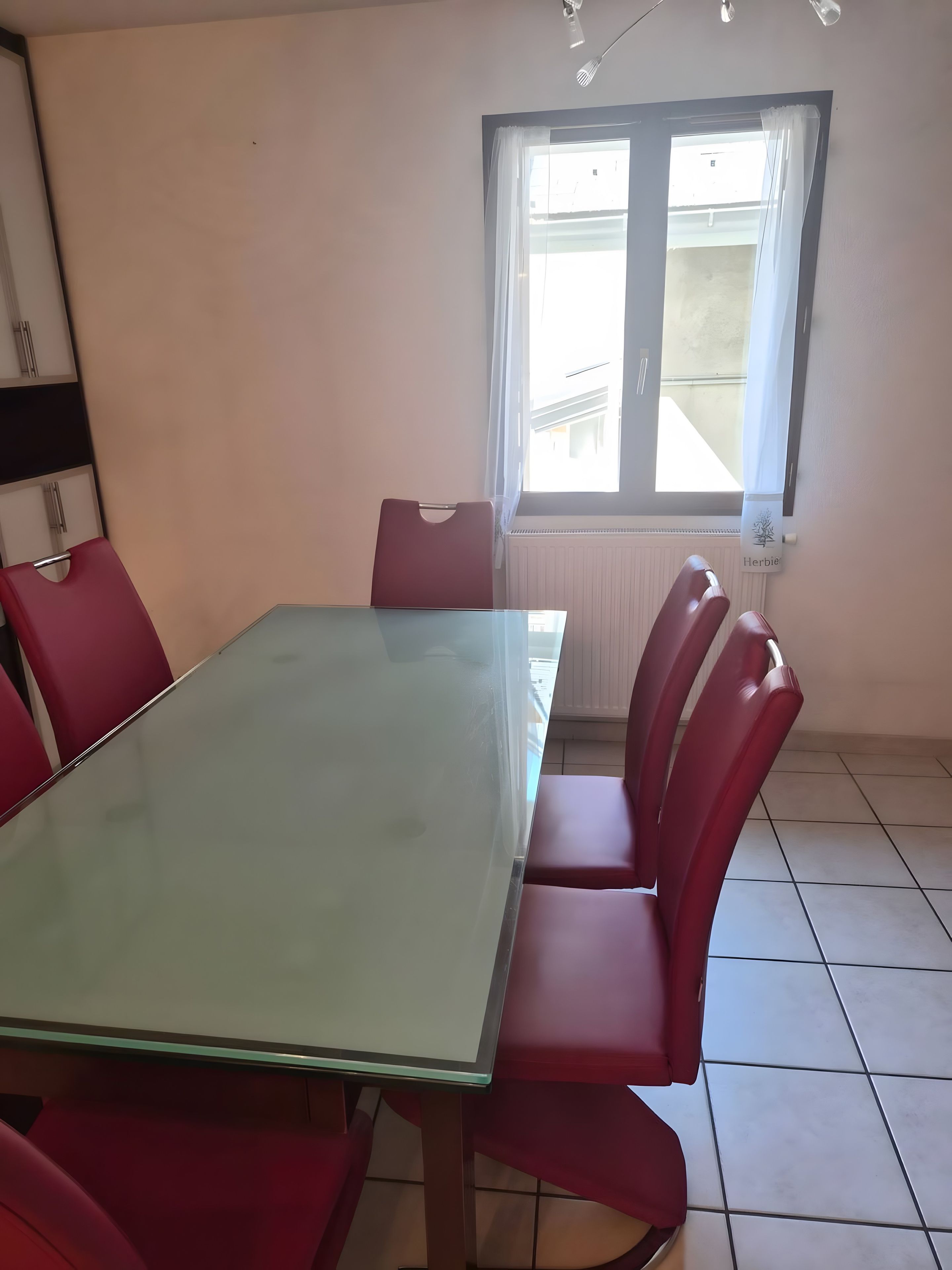 Una sala conferenze con tavolo in vetro e sedie rosse, una finestra con tende e un termosifone.