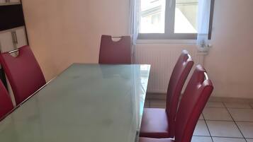 Una sala conferenze con tavolo in vetro e sedie rosse, una finestra con tende e un termosifone.