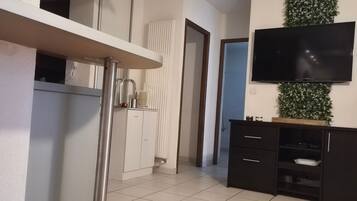Een moderne keuken met een wit aanrechtblad, een zwarte kast en een flatscreen televisie aan de muur.