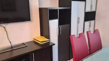 A modern kitchen with a flat-screen TV, a refrigerator, and a dining table with red chairs.