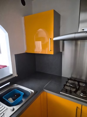 A kitchen with a gas stove, a sink with a blue container, and yellow cabinets.
