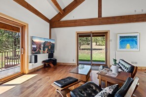 Una habitación amplia con piso de madera, un televisor de pantalla plana grande montado en la pared, un sofá de cuero y una mesa de vidrio.