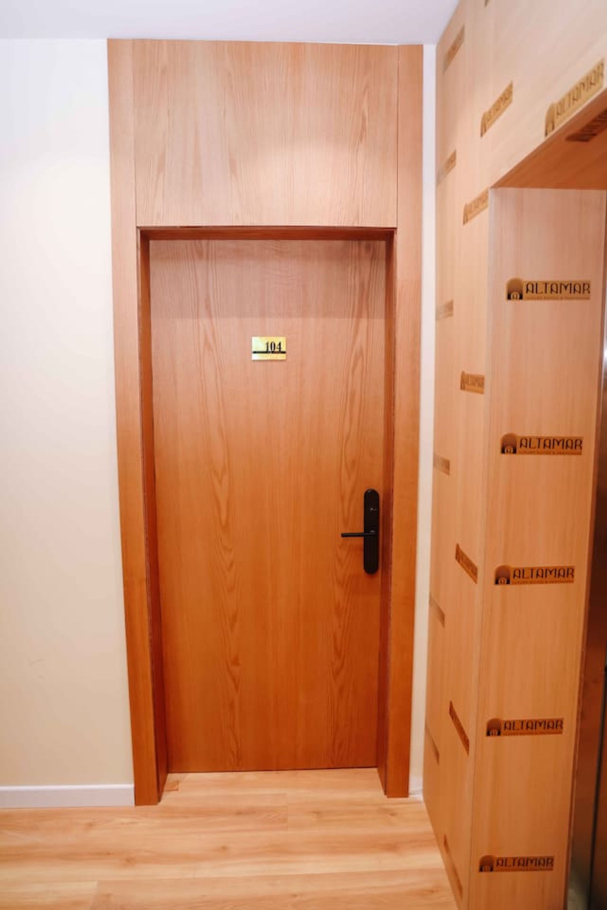 A wooden door with a number plate and a handle, leading to a room with a wooden floor.