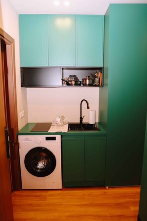 Cocina compacta con lavadora, lavamanos y encimera equipada con utensilios de cocina.