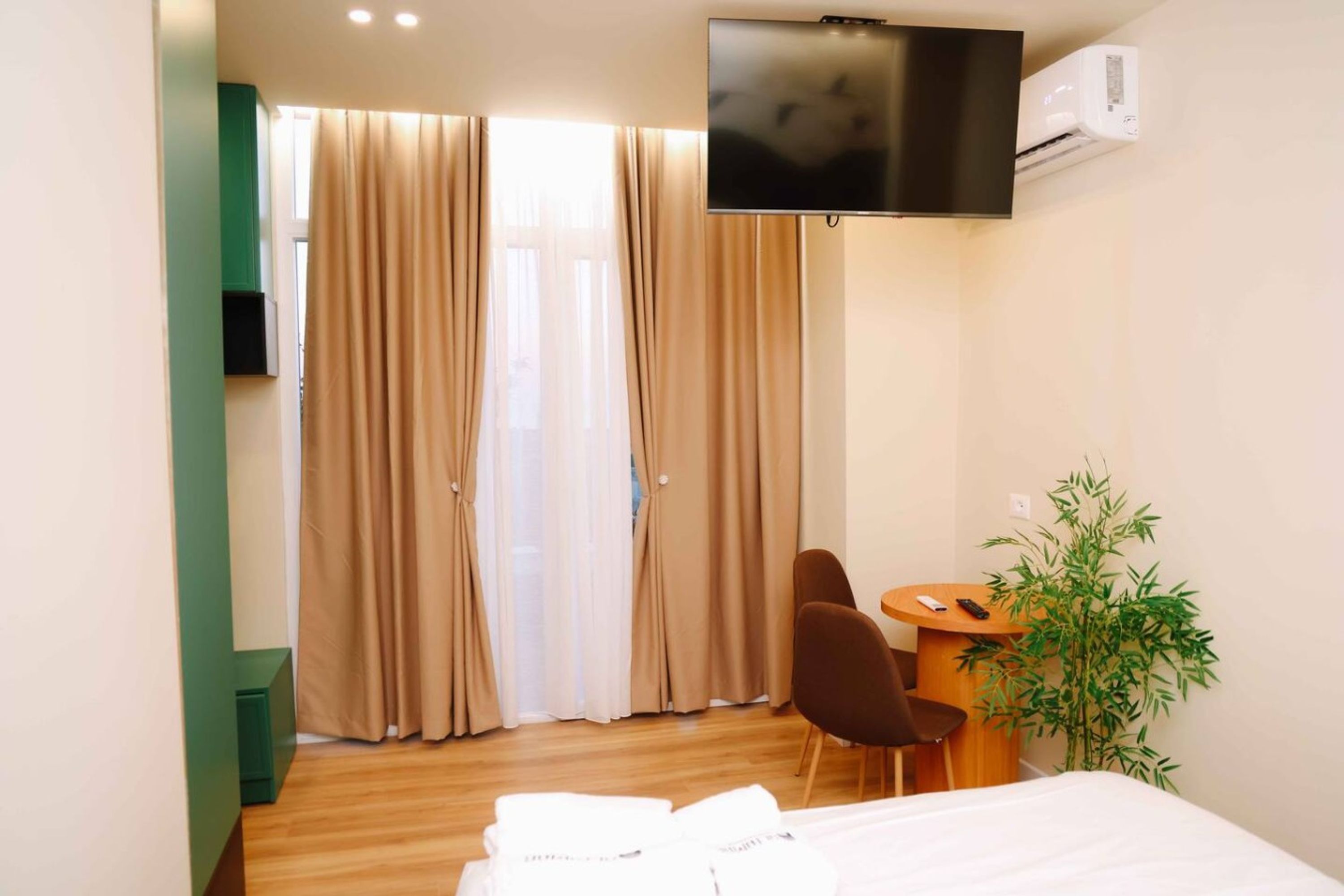 A hotel room with a bed, a TV mounted on the wall, a desk with a chair, and a plant.