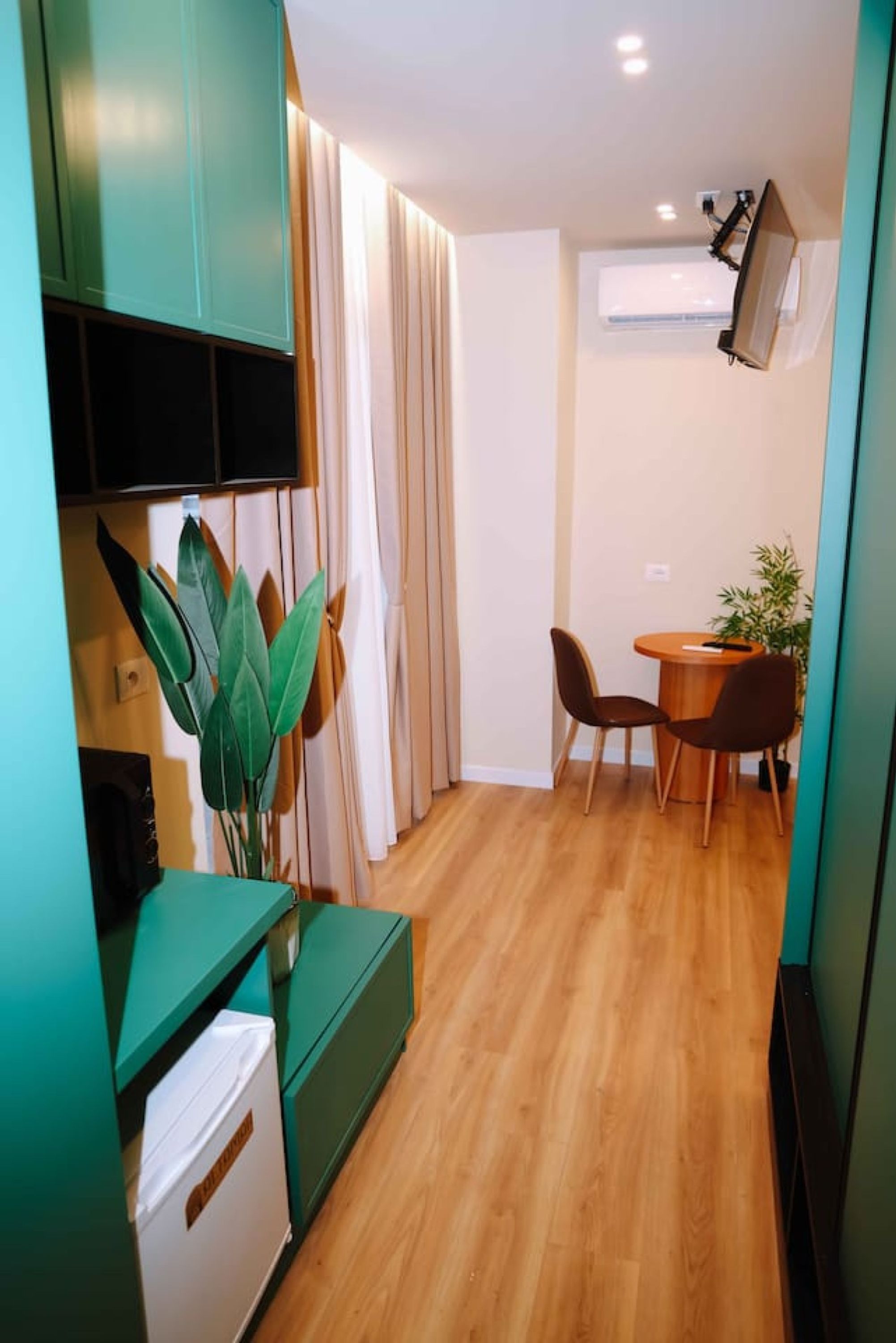 A compact living space with a kitchenette, a dining area with a table and chairs, and a large window with curtains.