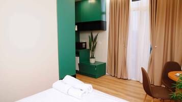 A hotel room with a bed, a green cabinet, a plant, a chair, and a table.