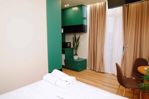 Une chambre d’hôtel avec un lit, une armoire verte, une plante, une chaise et une table.