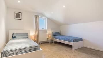 A bedroom with two beds, a window, a radiator, and a picture on the wall.