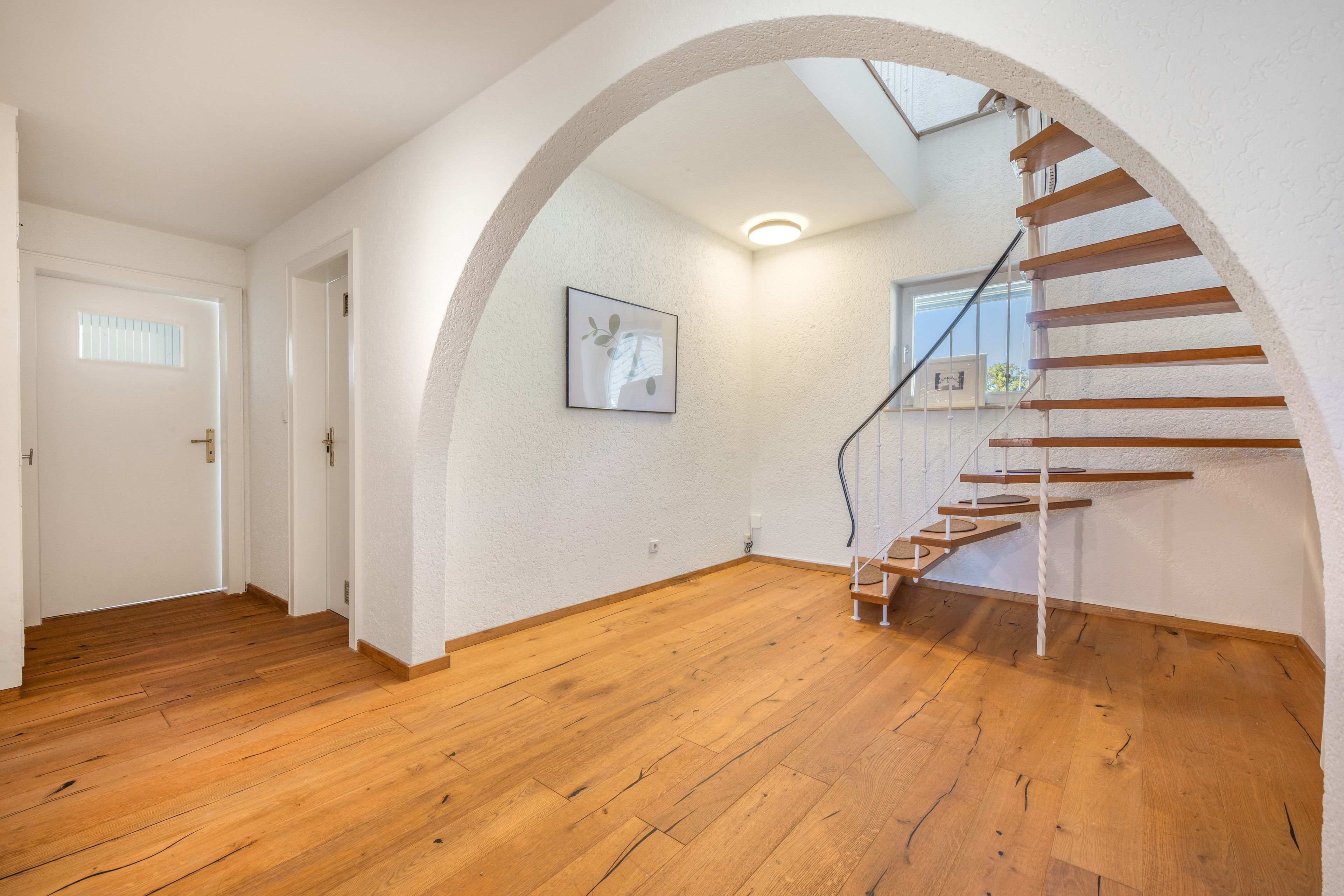 Ein geräumiger Raum mit Holzboden, einer weißen Tür und einer Treppe mit Holzstufen.