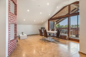 A spacious dining area with a high ceiling, a brick accent wall, and a view of the outdoors.
