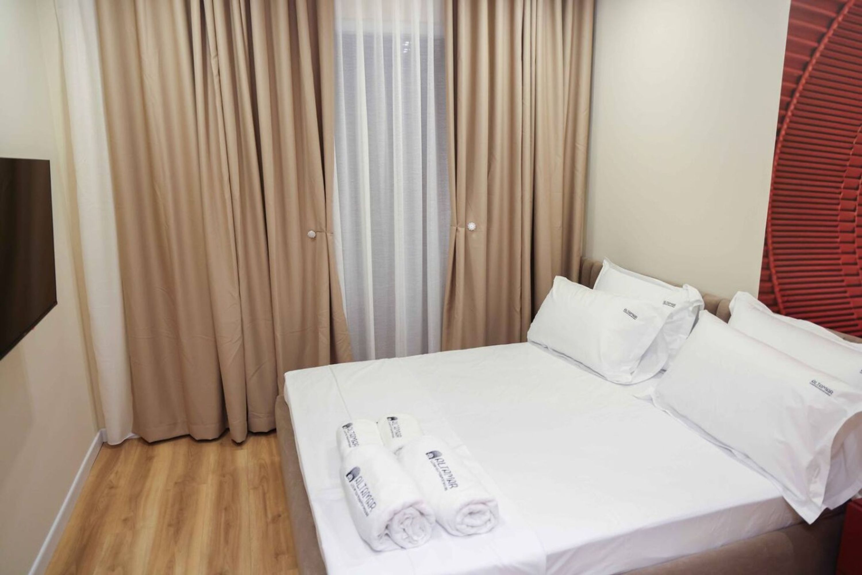 A hotel room with a bed, white linens, and a set of curtains.
