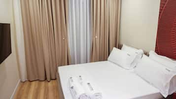 A hotel room with a bed, white linens, and a set of curtains.