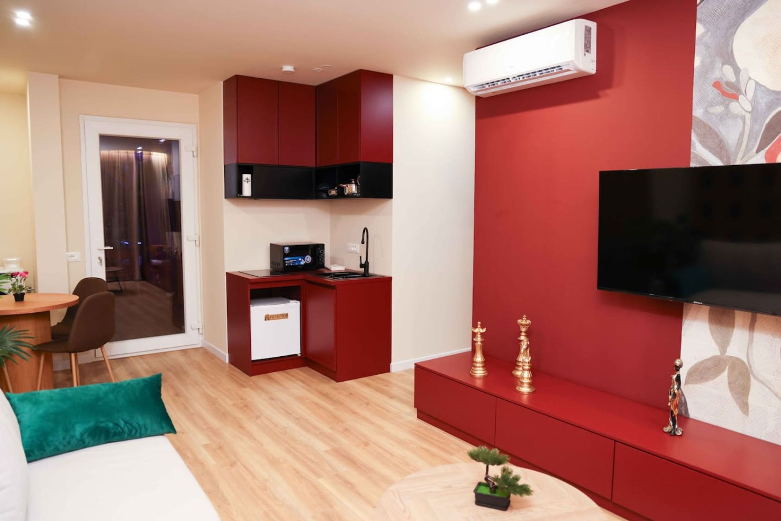 A compact living space with a kitchenette, a flat-screen TV mounted on the wall, and a small desk with a computer.
