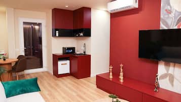 A compact living space with a kitchenette, a flat-screen TV mounted on the wall, and a small desk with a computer.