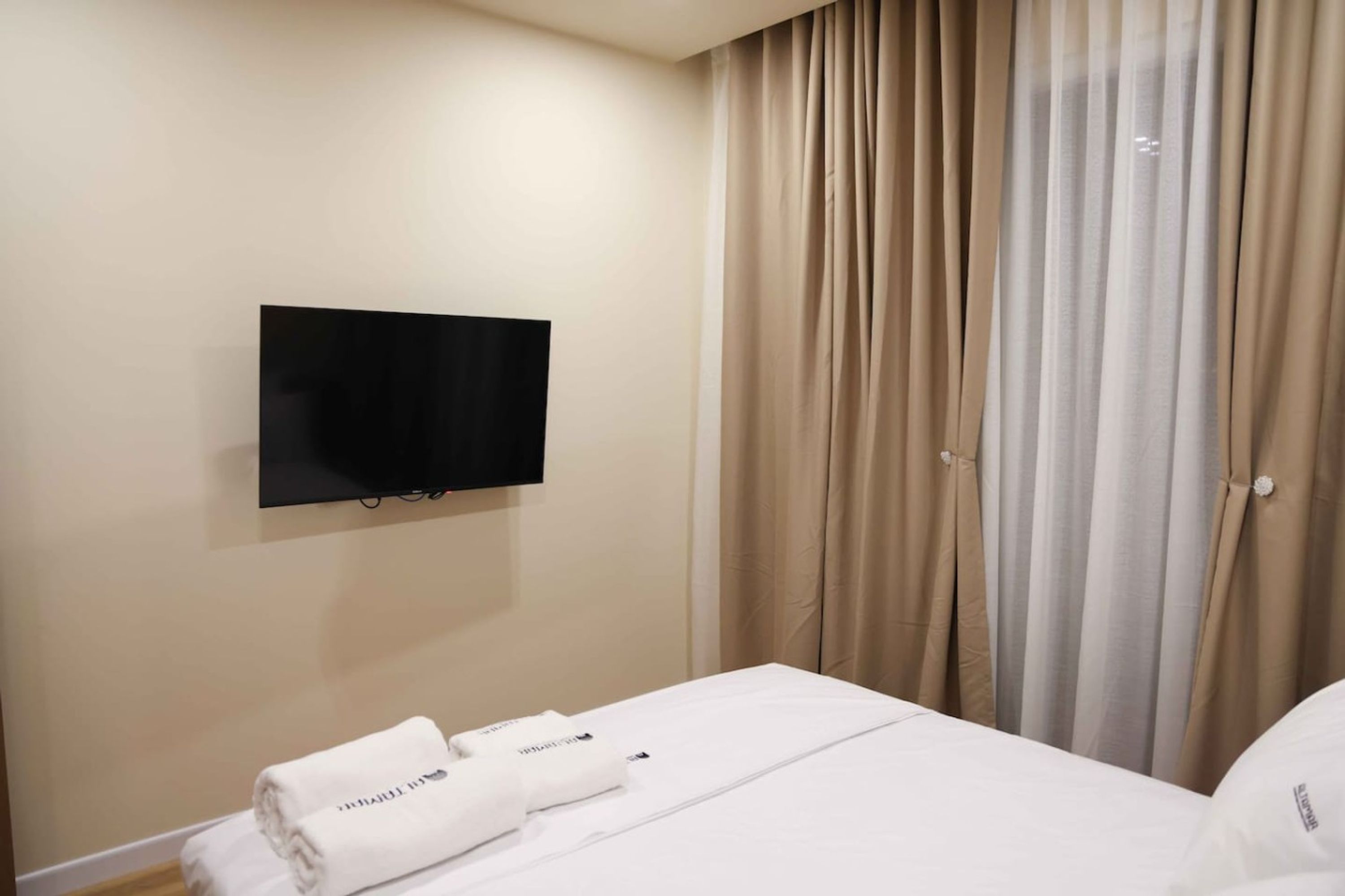 A hotel room with a bed, a flat-screen TV mounted on the wall, and a set of curtains.