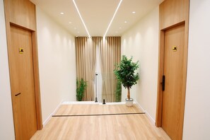 Pasillo de hotel con puertas de madera, una planta en maceta y un panel de vidrio.