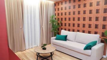 A living room with a white sofa, green cushions, a round coffee table, and a wooden wall panel.