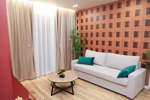 Una sala de estar con un sofá blanco, cojines verdes, una mesa de centro redonda y un panel de pared de madera.