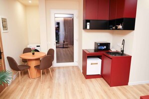 Un espacio habitable compacto con kitchenette, una zona de comedor con una mesa redonda y sillas, y vista a un dormitorio por una puerta abierta.