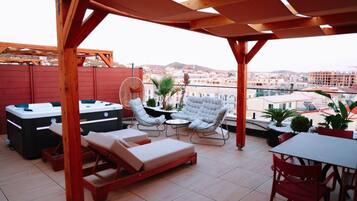 Una terraza en la azotea con una pérgola de madera, sillones de descanso, una mesa y un jacuzzi.