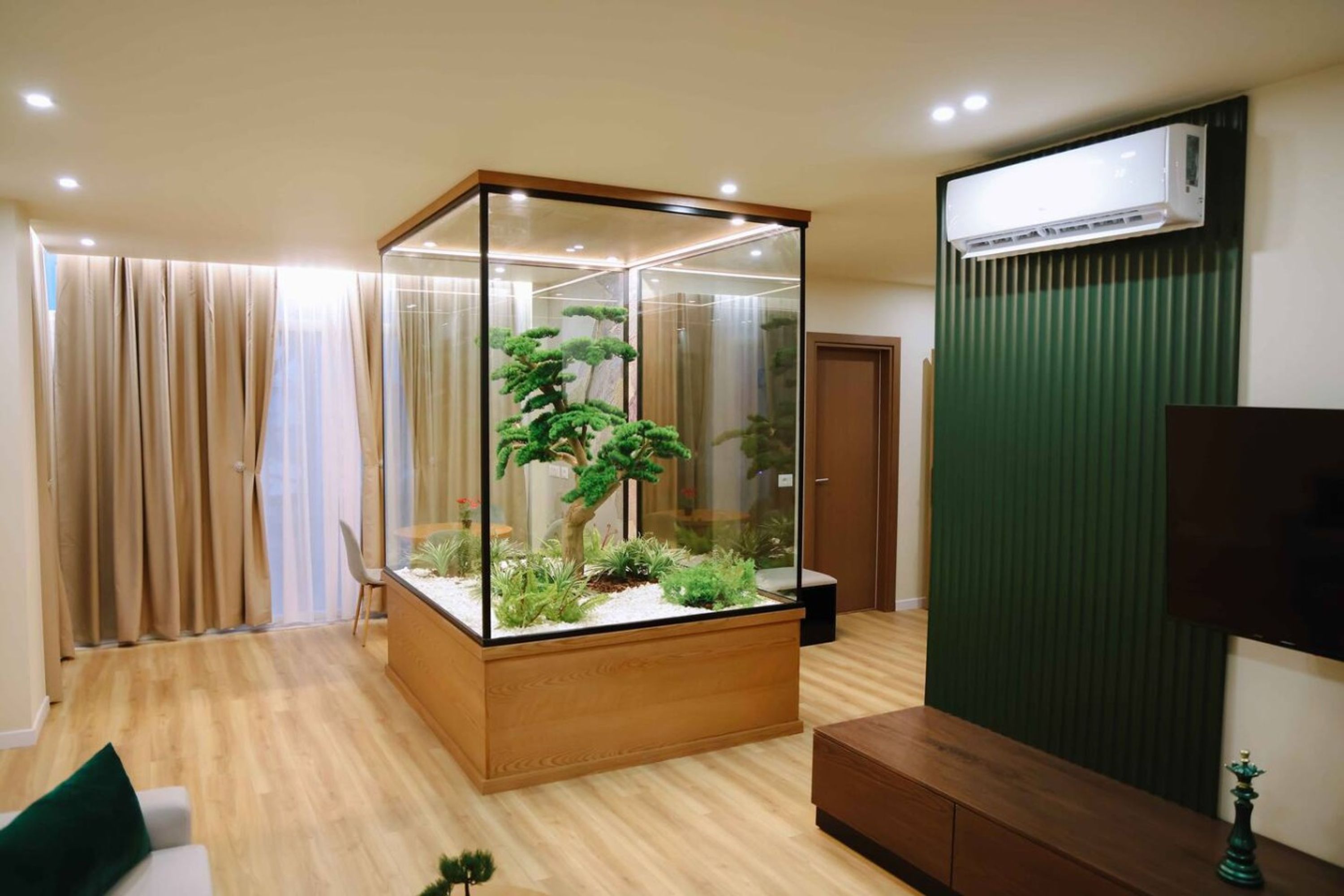 Una sala de estar moderna con un terrario de vidrio, piso de madera, un sofá y un televisor.