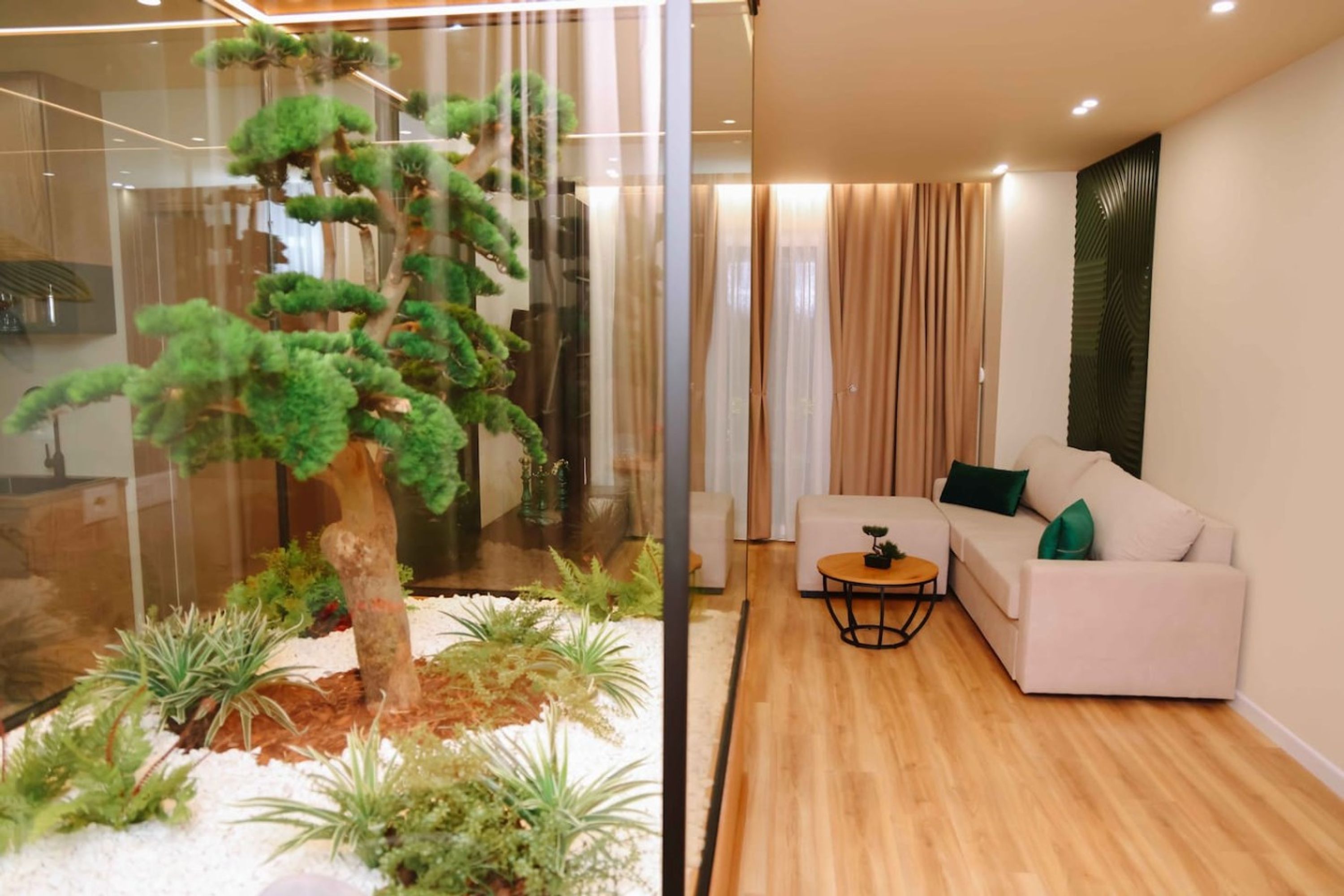 Una sala moderna con un separador de vidrio, un sofá blanco, una mesita redonda y un árbol bonsái.