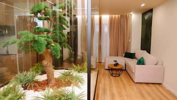 Una sala moderna con un separador de vidrio, un sofá blanco, una mesita redonda y un árbol bonsái.