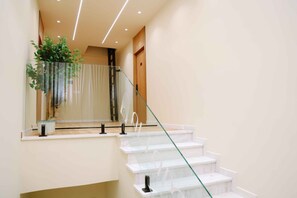 Uma escadaria moderna com guarda-corpos de vidro e um vaso de planta no patamar.