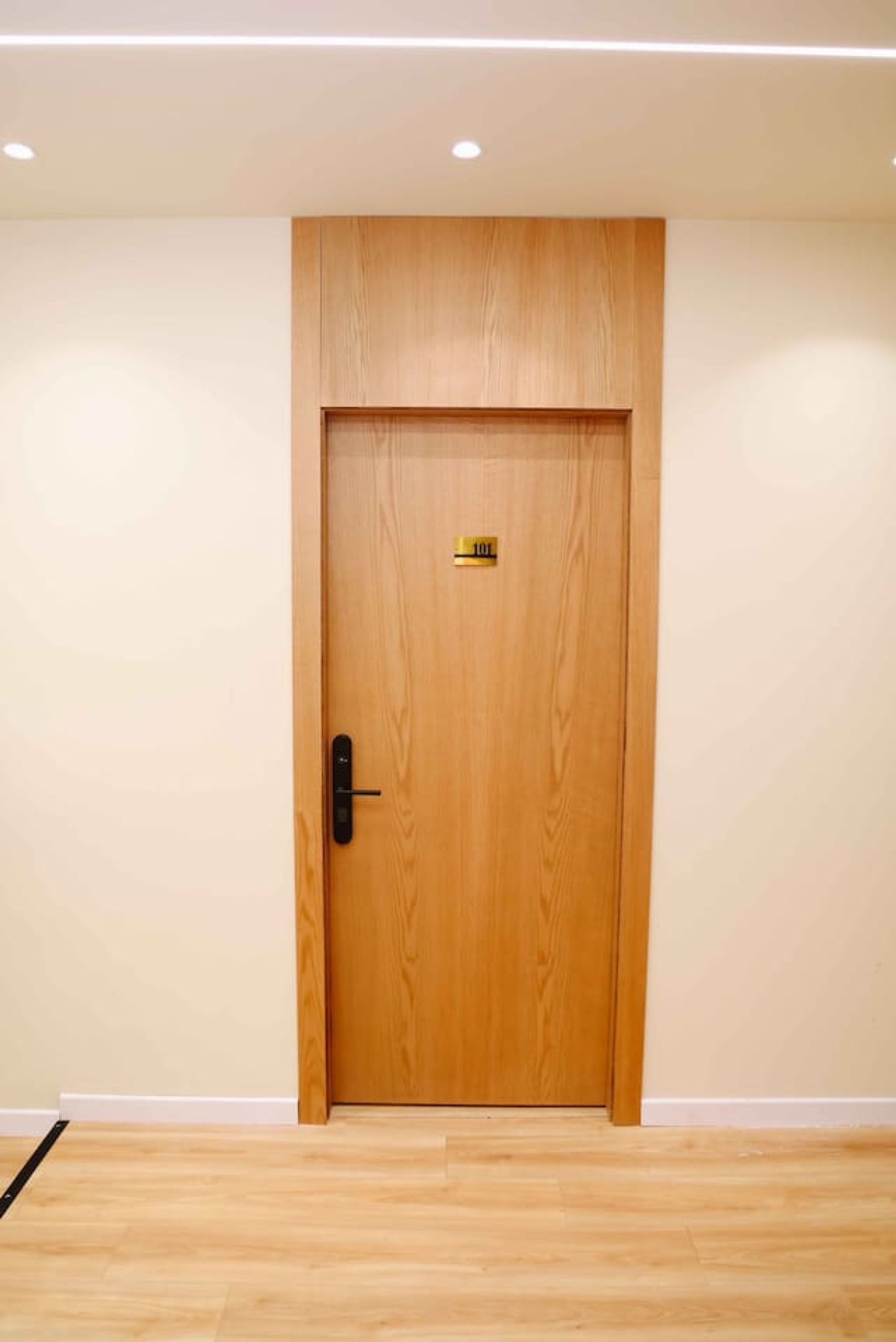 A wooden door with a keyhole and a small label, set in a room with a wooden floor and white walls.
