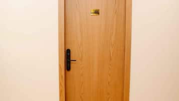 A wooden door with a keyhole and a small label, set in a room with a wooden floor and white walls.