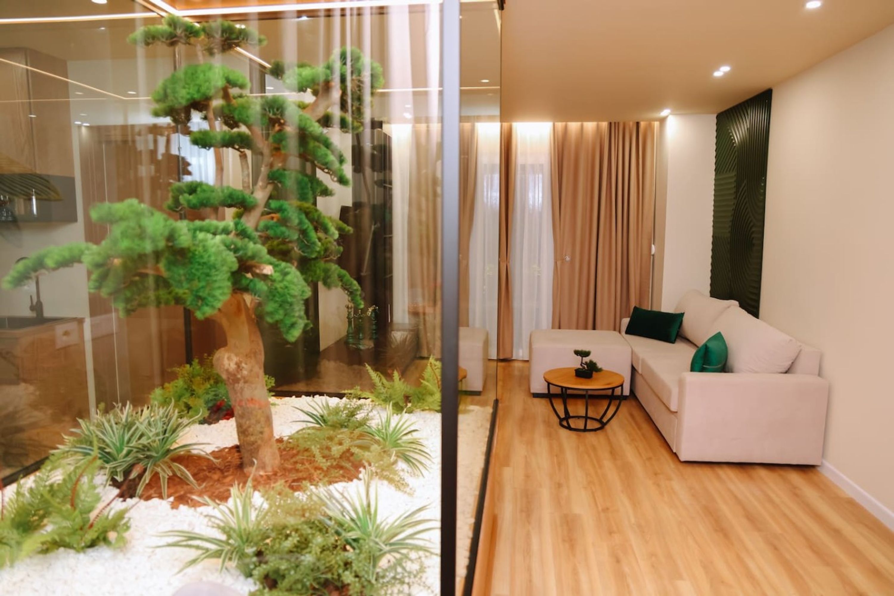 A modern living room with a glass partition, a white sofa, a small round table, and a bonsai tree.