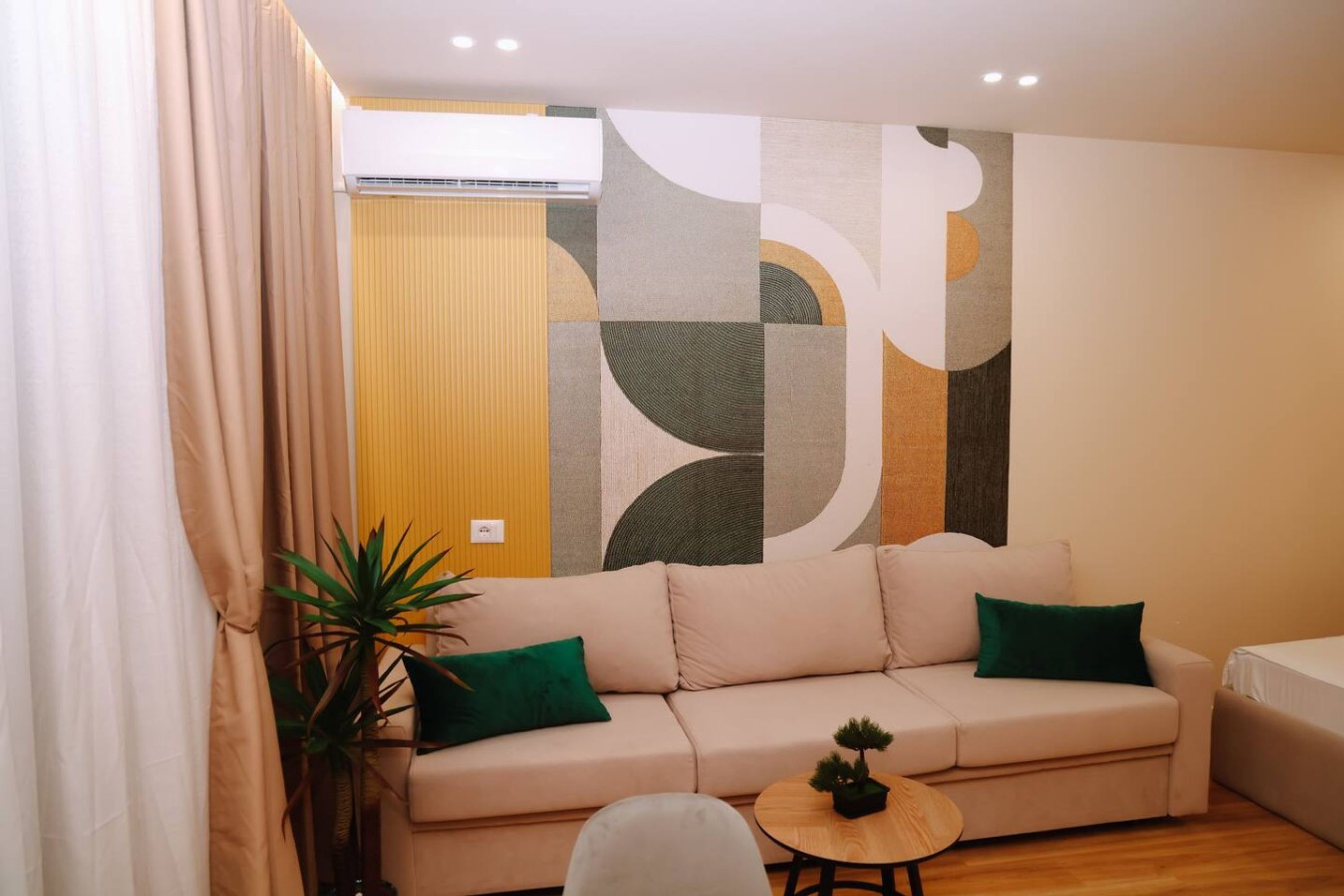 Ein modernes Wohnzimmer mit einem beigefarbenen Sofa, einem kleinen runden Holztisch und einer Zimmerpflanze.