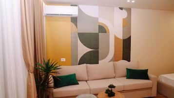 Ein modernes Wohnzimmer mit einem beigefarbenen Sofa, einem kleinen runden Holztisch und einer Zimmerpflanze.