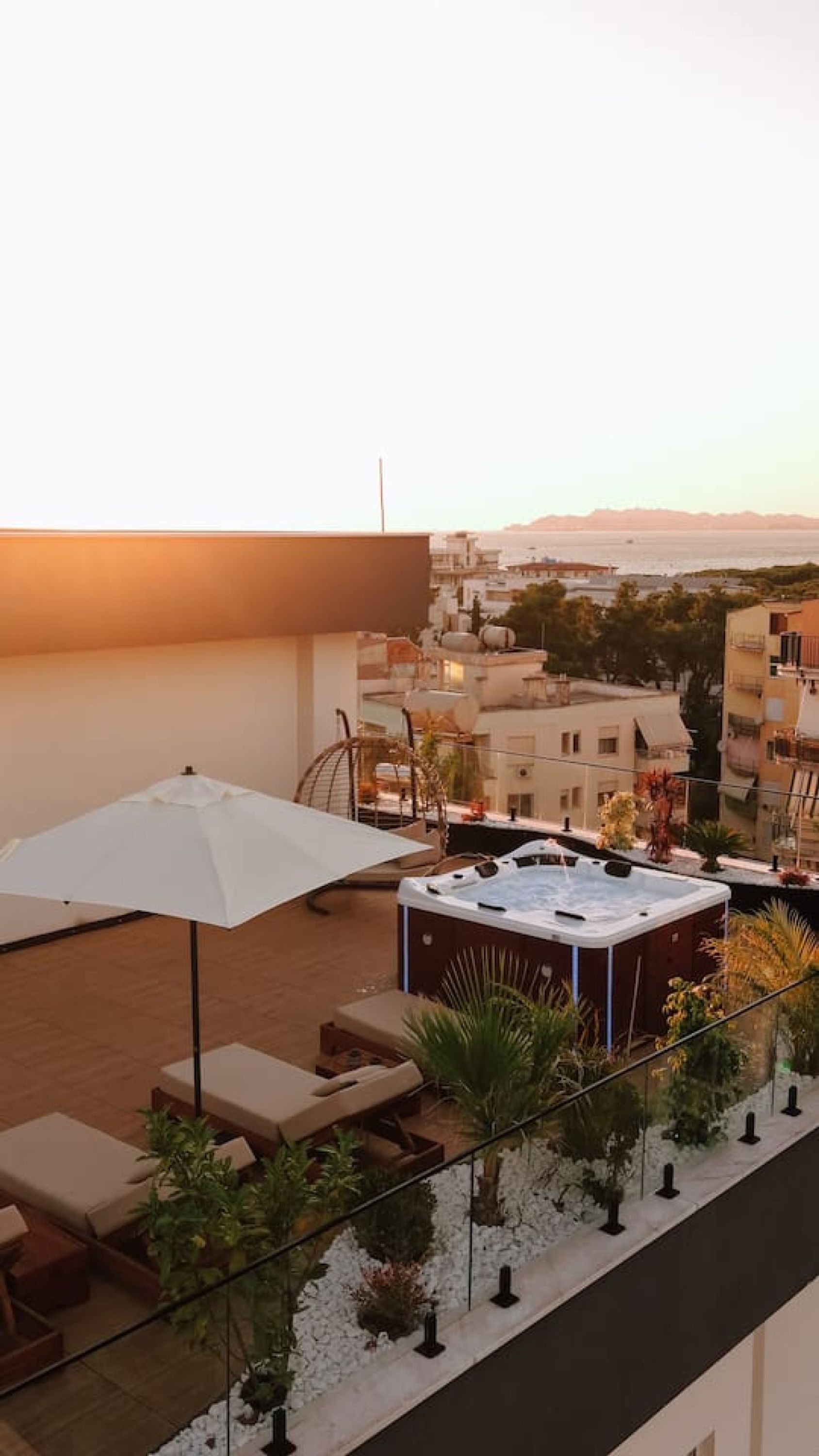Eine Dachterrasse mit Whirlpool, Liegestühlen und einem weißen Sonnenschirm.