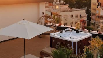 Eine Dachterrasse mit Whirlpool, Liegestühlen und einem weißen Sonnenschirm.