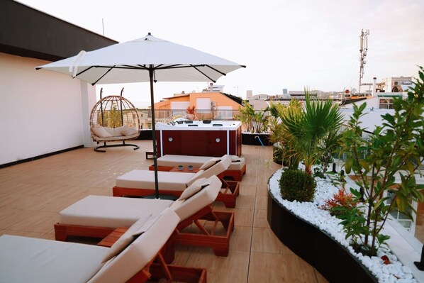 Una terraza en la azotea con tumbonas, una silla colgante, una parrilla y un gran toldo que da sombra.