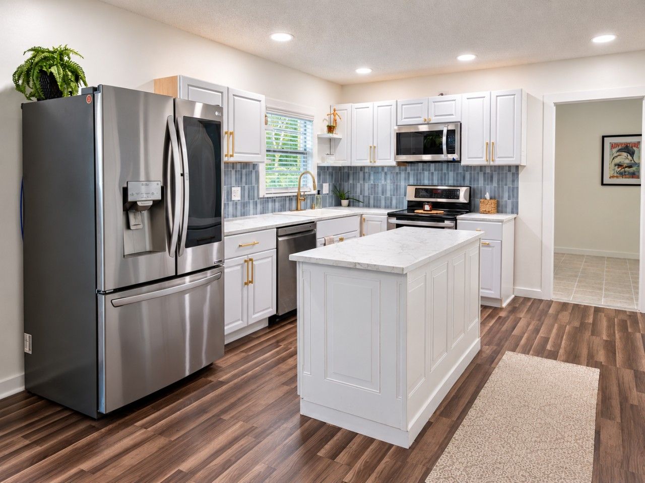 A modern kitchen with stainless steel appliances, white cabinetry, and a wooden floor.