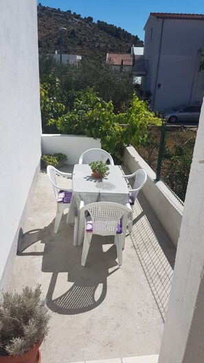 A small outdoor patio with a table and chairs, surrounded by greenery and a view of a hillside. - Spacious apartment with balcony, big garden & grill, near beach (Podglavica)
